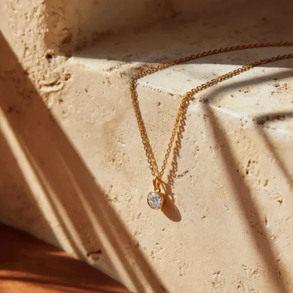 Fine gold chain with a lab-grown diamond pendant on ivory plaster